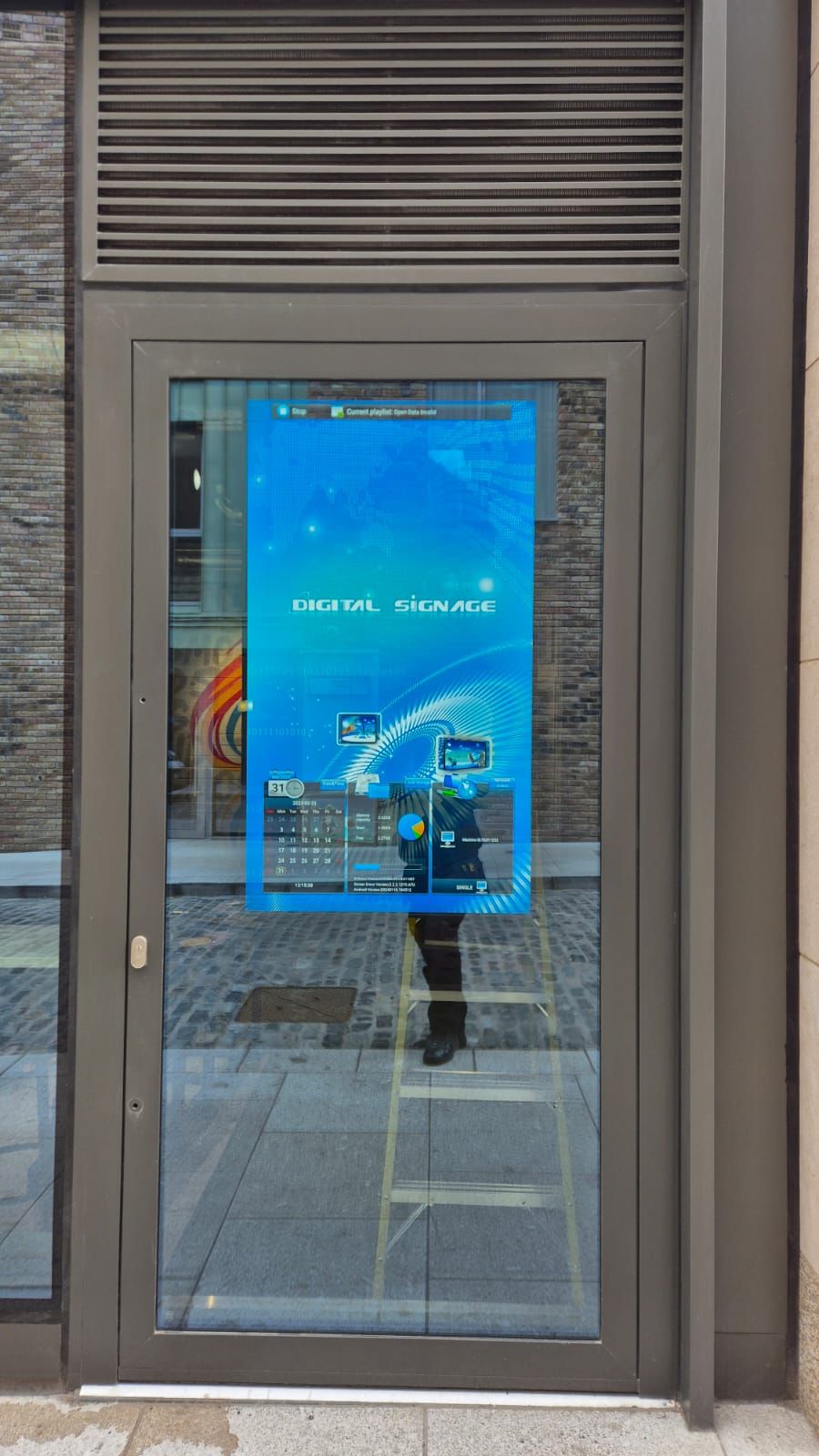 High brightness commercial display mounted behind storefront glass showing digital signage